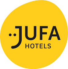 Żółte, okrągłe logo z napisem "JUFA HOTELS" w czarnym, stylizowanym tekście. Litery "JU" są częścią emotikonu. 